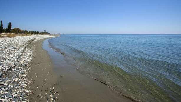 A pebble beach with clear water and a distant shoreline. - Larnaca Seaside Villa Marina 43 (Pervolia)