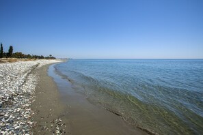Une plage de galets avec une eau claire et une côte visible au loin.
