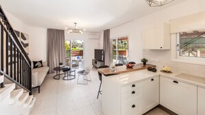 A modern kitchen with white cabinets, a wooden countertop, and a built-in oven. There is a dining area with a table and chairs, and a staircase leading to another level. - Larnaca Seaside Villa Marina 44 (Pervolia)