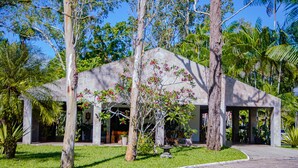 A modern building with a sloped roof, surrounded by lush greenery and palm trees. - Casa c Wifi Churrasq Pisc red rio Pet Friendly (Benevides)