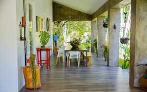 A spacious indoor area with a wooden floor, a dining table with chairs, and various potted plants.