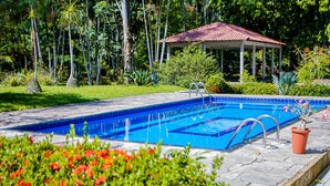 A swimming pool with a tiled deck, surrounded by lush greenery and a gazebo. - Casa c Wifi Churrasq Pisc red rio Pet Friendly (Benevides)