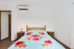 Une chambre à coucher avec un lit en bois, une table de chevet, une lampe et un climatiseur fixé au mur.