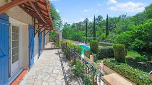 A stone-paved balcony with a wooden pergola, a swimming pool, and lush greenery. - Villa in Flayosc With Private Pool (Flayosc)