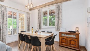 A dining area with a wooden table and black chairs, a wooden cabinet with a telephone, and a window with curtains. - Villa in Flayosc With Private Pool (Flayosc)