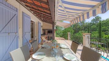 An outdoor dining area with a table set for four, surrounded by wicker chairs, under a striped awning.