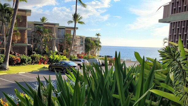 Un hotel sulla costa con vista sull'oceano, caratterizzato da architettura moderna, un'area di parcheggio e una vegetazione rigogliosa.
