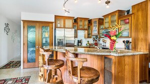Una cucina con mobili in legno, una grande isola con sgabelli, un frigorifero e un vaso con fiori.