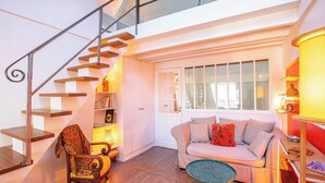 Una sala de estar acogedora con una escalera, un sofá, una silla y una mesita.