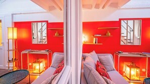 Un cuarto con espejo, pared roja, sofá y una mesa con lámpara.