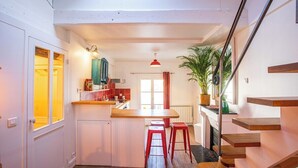 Cocina compacta con isla central, taburetes rojos y una escalera de madera.