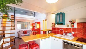 Una cocina moderna con encimera de madera, azulejos rojos y un horno empotrado. Hay una zona de comedor con taburetes rojos y un sofá.