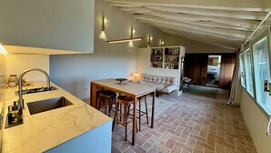 A kitchen with a marble countertop, a sink, and a dining area with stools. There is a bookshelf and a sofa in the background. - Haven of peace in the Garraf: 18th-century masia, sea view & exceptional light (Olivella)