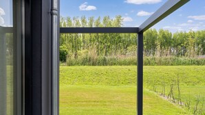 Une terrasse en bois avec une rambarde en métal, donnant sur un champ herbeux et des arbres.