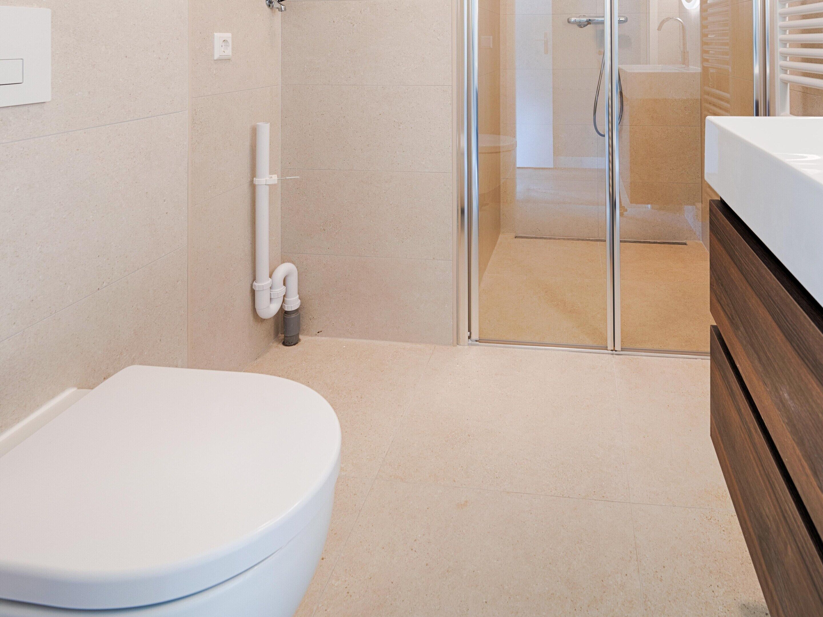 Een moderne badkamer met toilet, douche en douchecabine met glazen wanden.