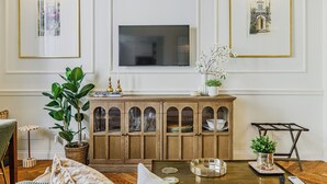 Een woonkamer met een houten kast, een televisie en kunstwerken in lijsten aan de wanden.