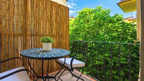 Een klein terras buiten met een ronde tafel en een stoel, een bamboescherm en weelderige begroeiing op de achtergrond.