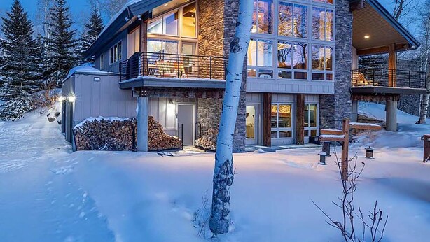 A modern two-story house with large windows, a stone facade, and a snow-covered landscape.