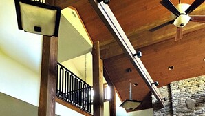 A spacious interior with a stone fireplace, a wooden staircase, and a ceiling fan.