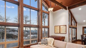 A spacious living room with large windows, a wooden ceiling, and a cozy sectional sofa.