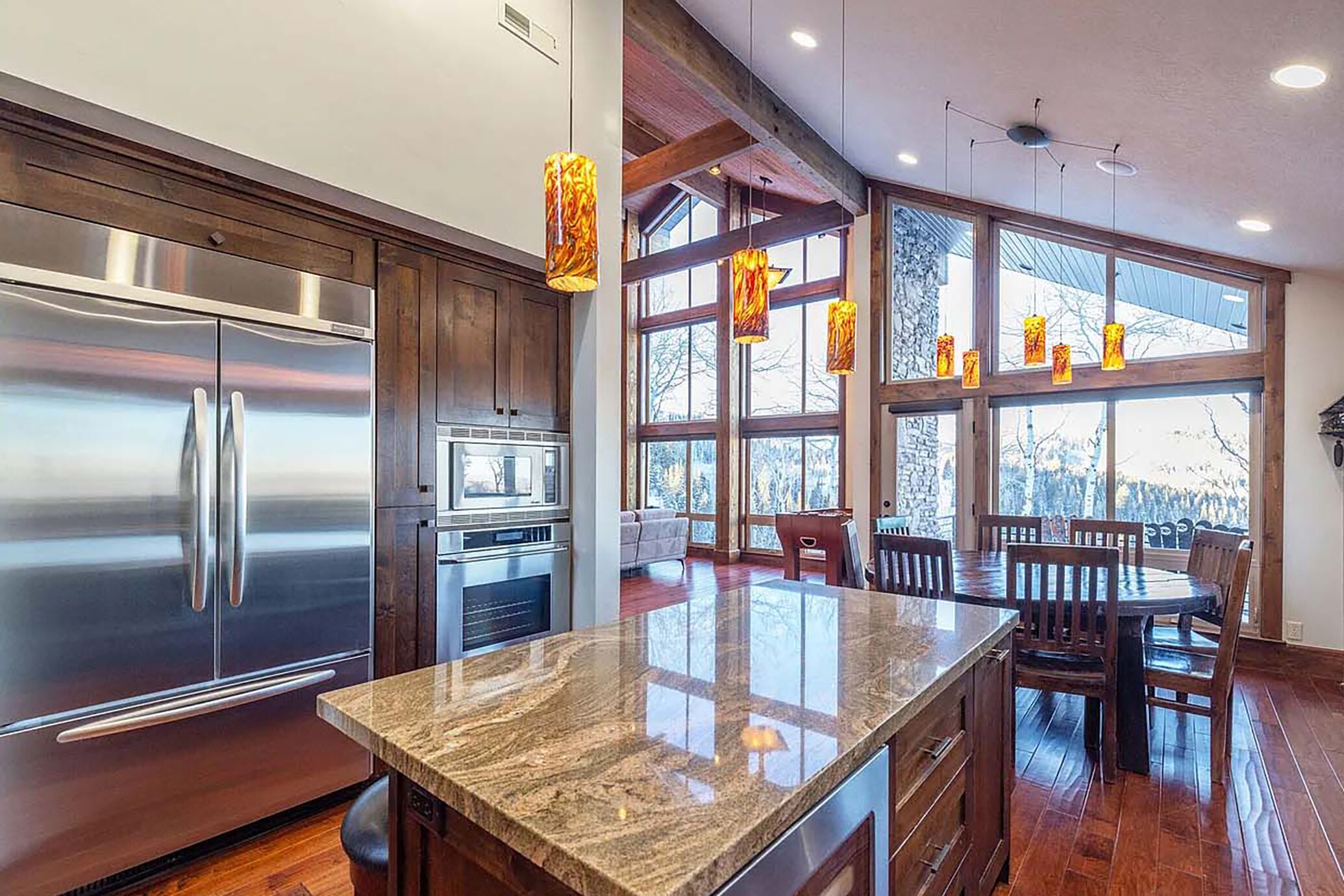 A modern kitchen with stainless steel appliances, a granite countertop, wooden flooring, and large windows with a view.