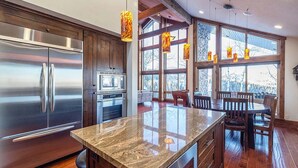 A modern kitchen with stainless steel appliances, a granite countertop, wooden flooring, and large windows with a view.