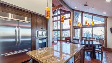 A modern kitchen with stainless steel appliances, a granite countertop, wooden flooring, and large windows with a view.
