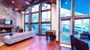 A spacious living room with a stone fireplace, large windows, and a pool table.