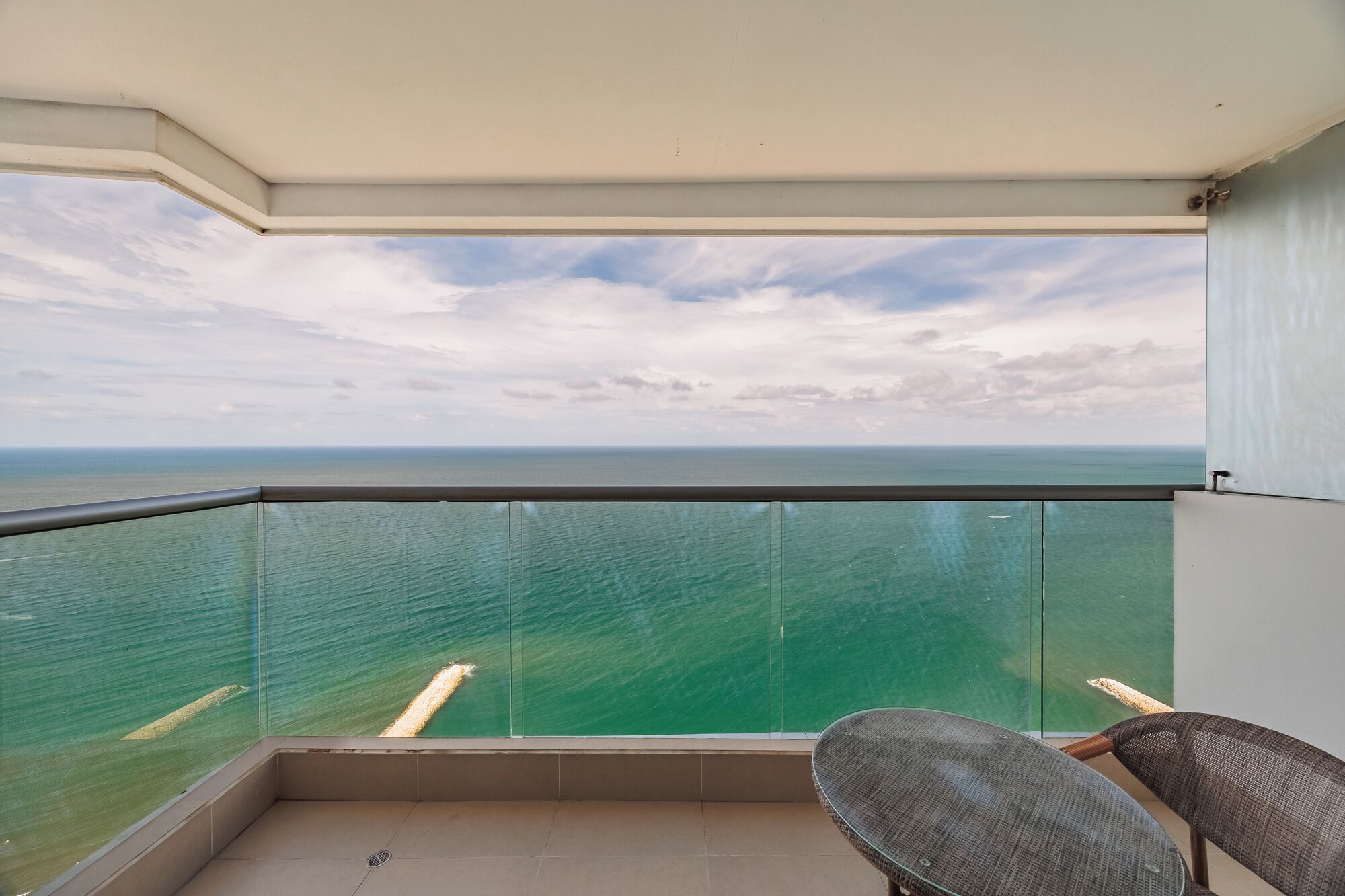 Uma varanda com guarda-corpo de vidro, uma cadeira e vista para o horizonte.