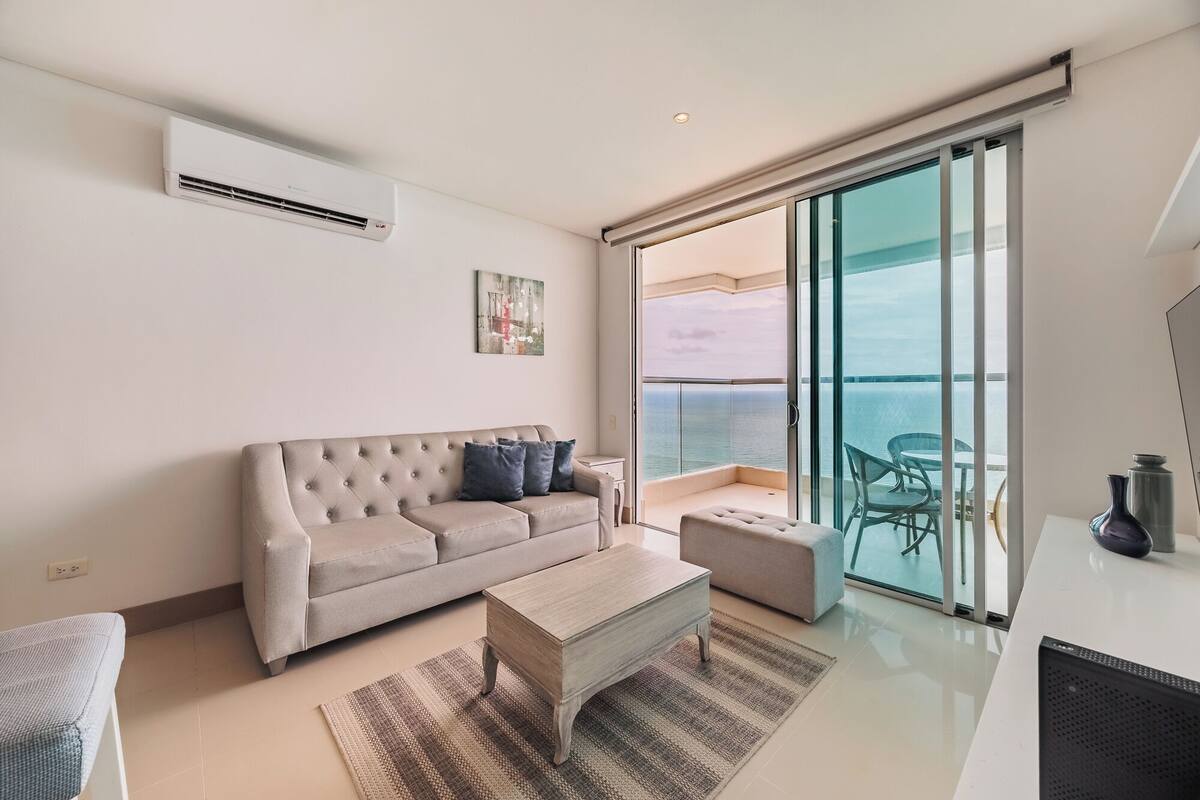 A modern living room with a sofa, a coffee table, and a view of the ocean through large glass doors.