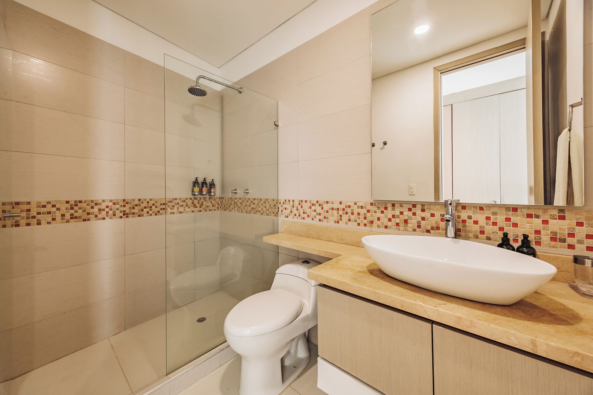 A modern bathroom with a glass shower enclosure, a white toilet, and a large sink with a beige countertop.