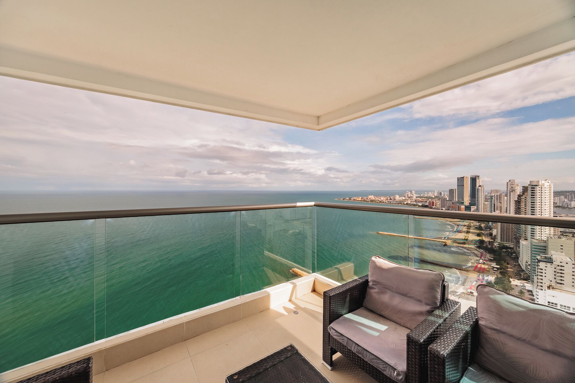 Ein Balkon mit Glastrennwand, der auf eine Stadtlandschaft und das Meer blickt.