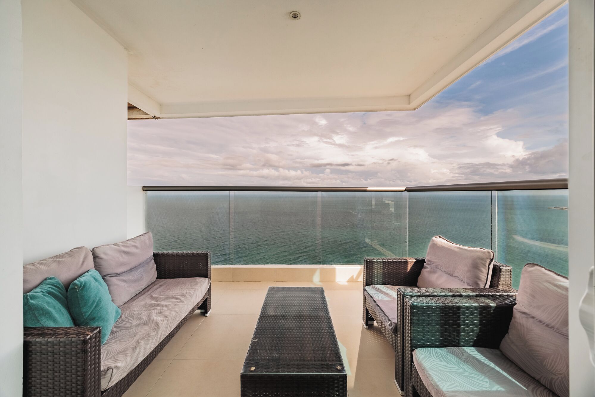 A balcony with wicker furniture, a glass barrier, and a view of the sea.