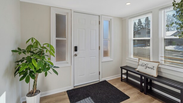 A clean, modern entryway with a white door, a potted plant, a bench with a cushion, and a black rug. - Charming 3-bedroom house in North Syracuse (North Syracuse)