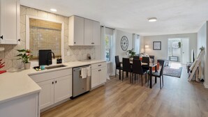 A modern kitchen with white cabinets, a built-in dishwasher, and a dining area with a table and chairs. - Charming 3-bedroom house in North Syracuse (North Syracuse)