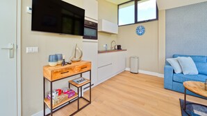 Een modern appartement met een keuken, een woonruimte met een blauwe bank, een houten salontafel en een aan de muur bevestigde televisie.