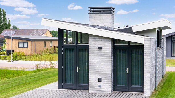 Een modern huis met een plat dak, grote glazen deuren en een houten terras.