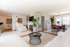Un salón amplio con un sofá blanco, una mesa de centro y una chimenea. Hay un comedor con una mesa y sillas de madera.