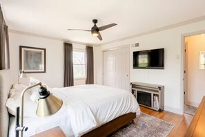 Una habitación de hotel con cama, escritorio con lámpara, televisor, chimenea y ventilador de techo.