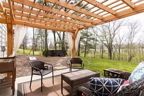 Un patio exterior con mobiliario de mimbre, una pérgola y vistas a zona boscosa.
