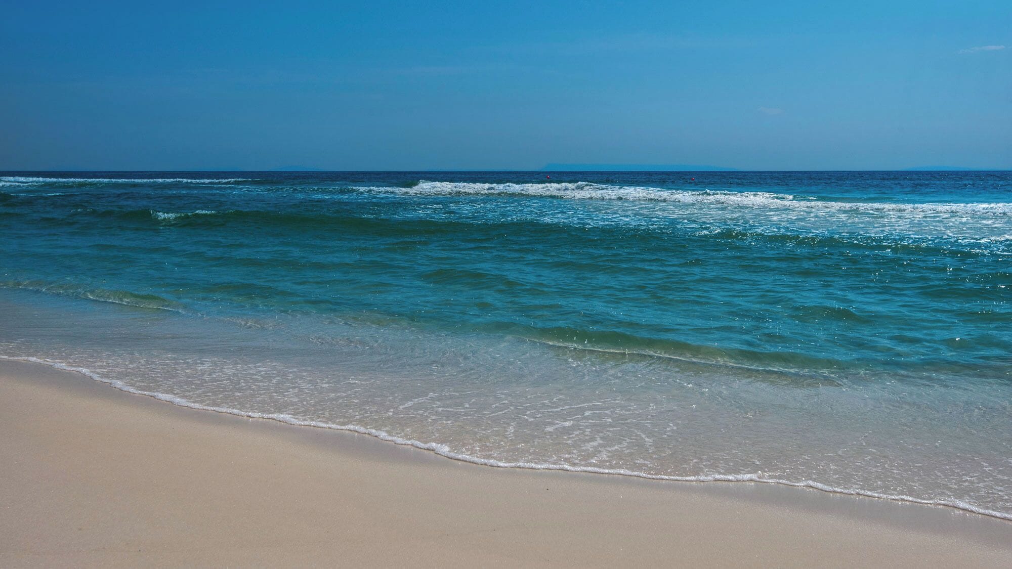 A beach with clear blue water and a sandy shore.
