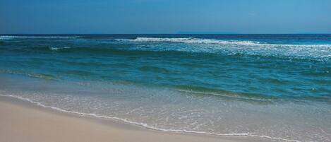 A beach with clear blue water and a sandy shore.