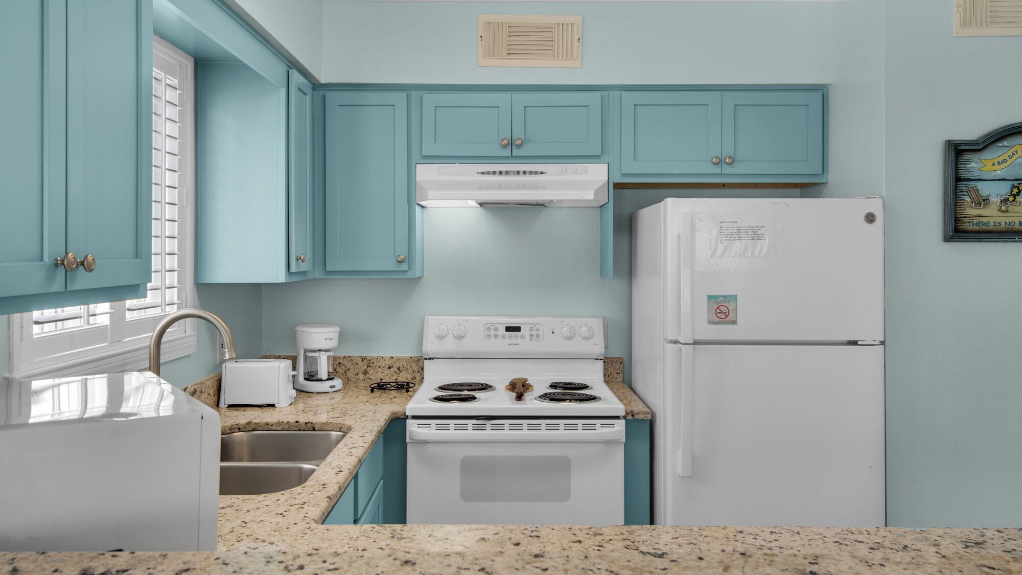 A kitchen with teal cabinets, a white stove, a white refrigerator, and a coffee maker.