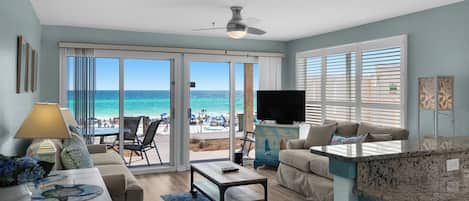 Una sala de estar con vista a la playa, un ventilador de techo, un televisor y un comedor.