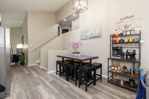 Una cocina moderna con una mesa de madera, taburetes negros, una estación de café y una escalera que sube a otro nivel.