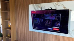 Televisió penjada a la paret sobre una superfície de marbre amb fons de panell de fusta.