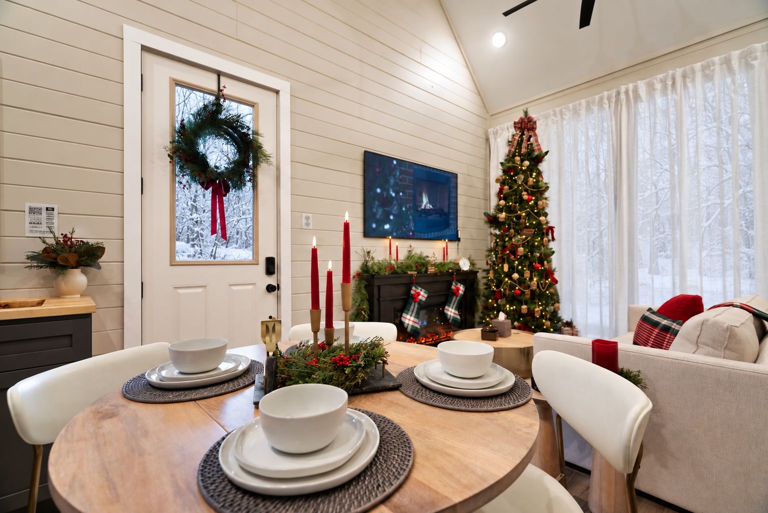 Un coin repas avec une table en bois dressée pour quatre personnes, un sapin de Noël et une cheminée décorée de chaussettes.