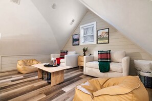 A loft-style living room with a sloped ceiling, wooden flooring, and a mix of seating including a sofa and bean bags.