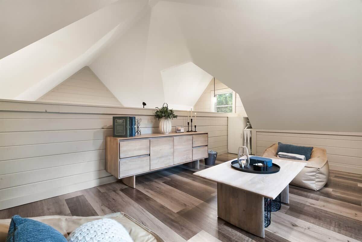 Una habitación estilo loft con techo inclinado, un armario de madera, una mesa de comedor y un sillón de peluche.