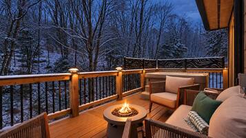 Una terraza con mobiliario exterior, un hogar para la leña y vistas a un bosque nevado.